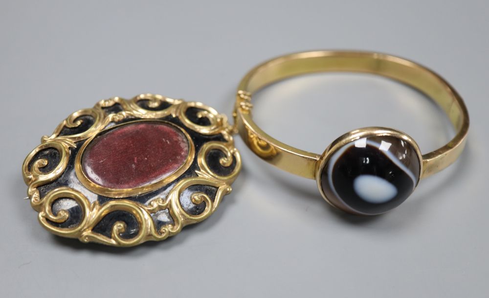 An early 20th century yellow metal (stamped 15) and banded agate set hinged bangle (repaired) and a Victorian mourning brooch.
